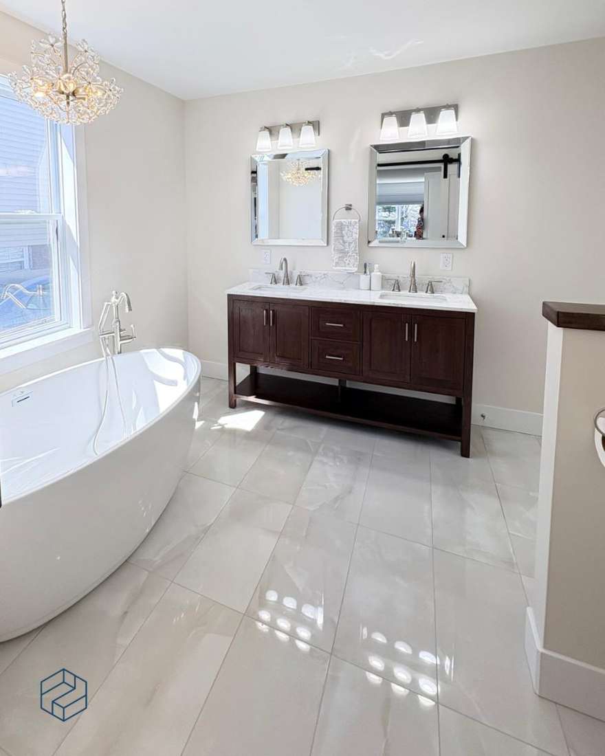 Wide view of the finished Albany primary bathroom — freestanding soaking tub, dark-wood double vanity, and marble-look porcelain floor.